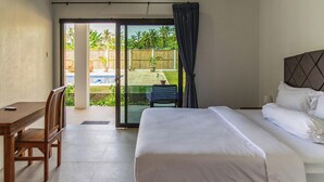Habitación de hotel con cama, escritorio y vista a un patio con piscina y palmeras.