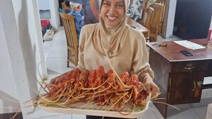 Una persona llevando una bandeja con langostas cocidas en una habitación con suelo de baldosas, muebles de madera y un ventanal grande.