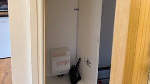 A narrow hallway with a white door on the left, a white wall with a black hanger on the right, and a small white box on the floor. - Rustic Roost: Countryside, Warm Cabin w/ Countryside Views & King Bed (Maybole)