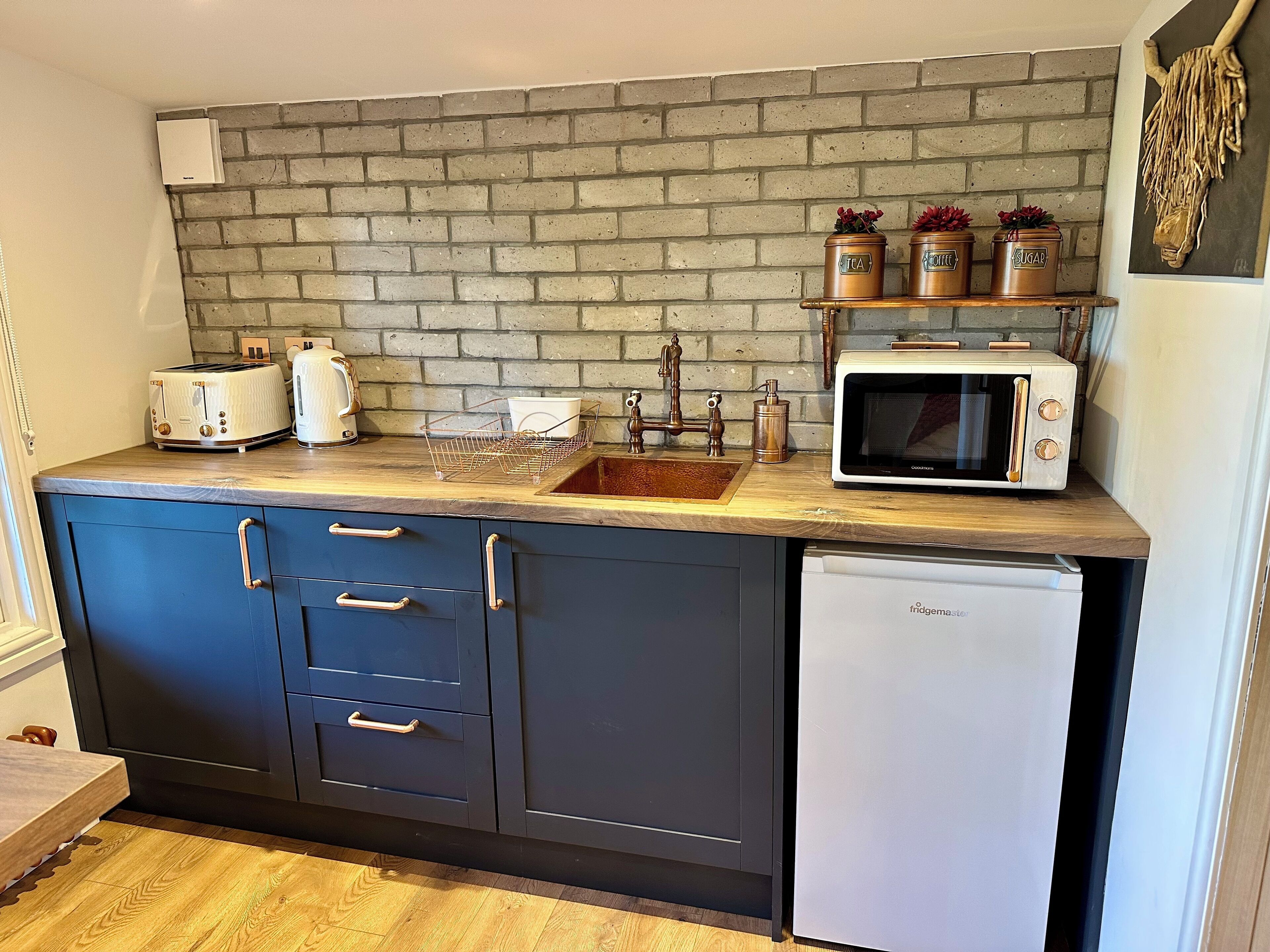 A kitchen with a brick backsplash, a sink, a microwave, a toaster, and a refrigerator.