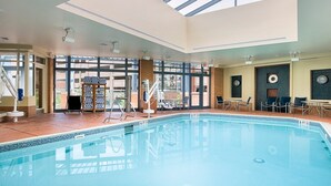 An indoor swimming pool with clear glass ceiling, poolside chairs, and a sunlit room with a view. - Club Wyndham National Harbor (Oxon Hill)