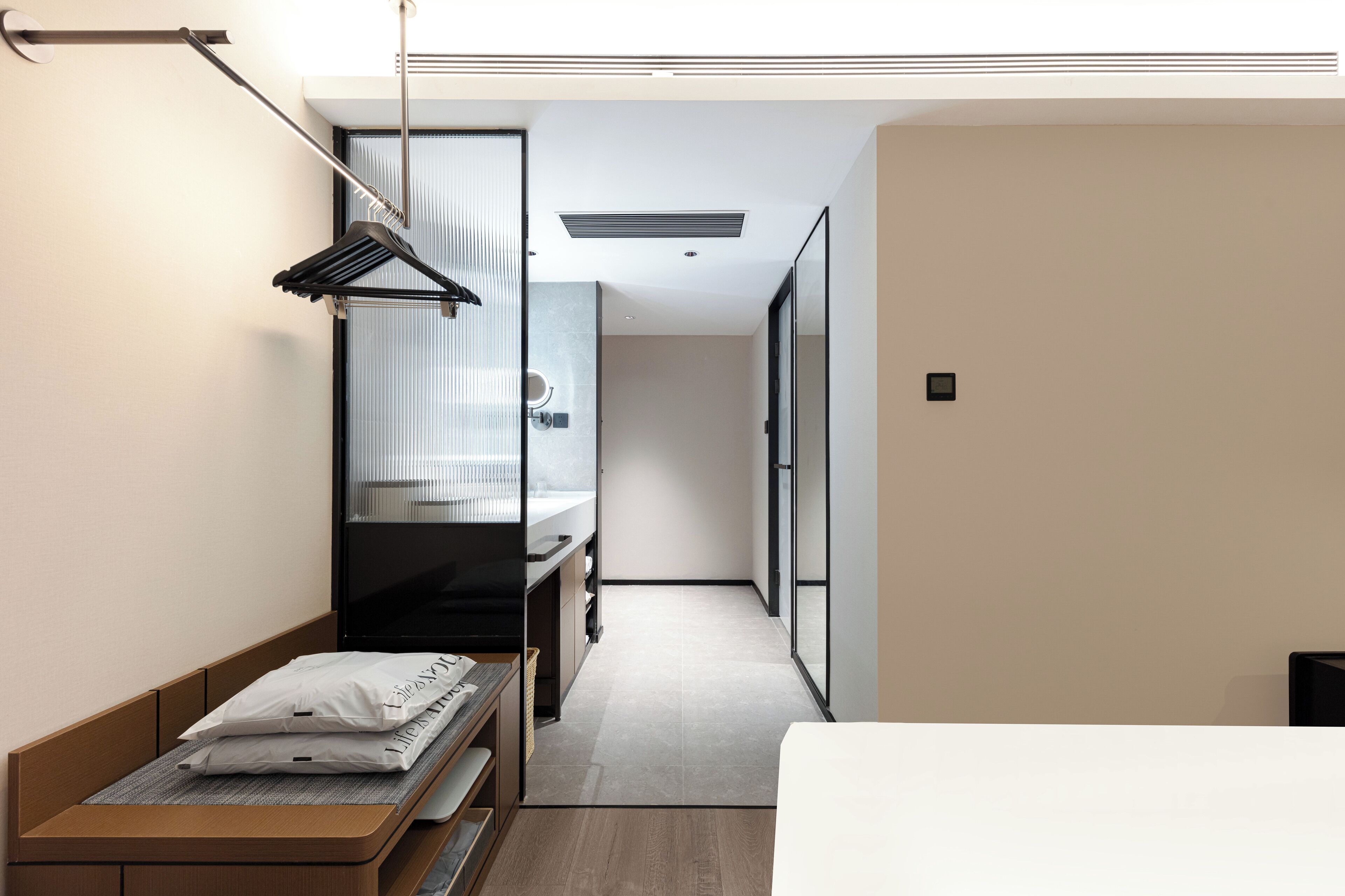 Une chambre d’hôtel moderne avec un lit en bois, un petit bureau, un porte-serviettes mural et une vue sur le couloir.