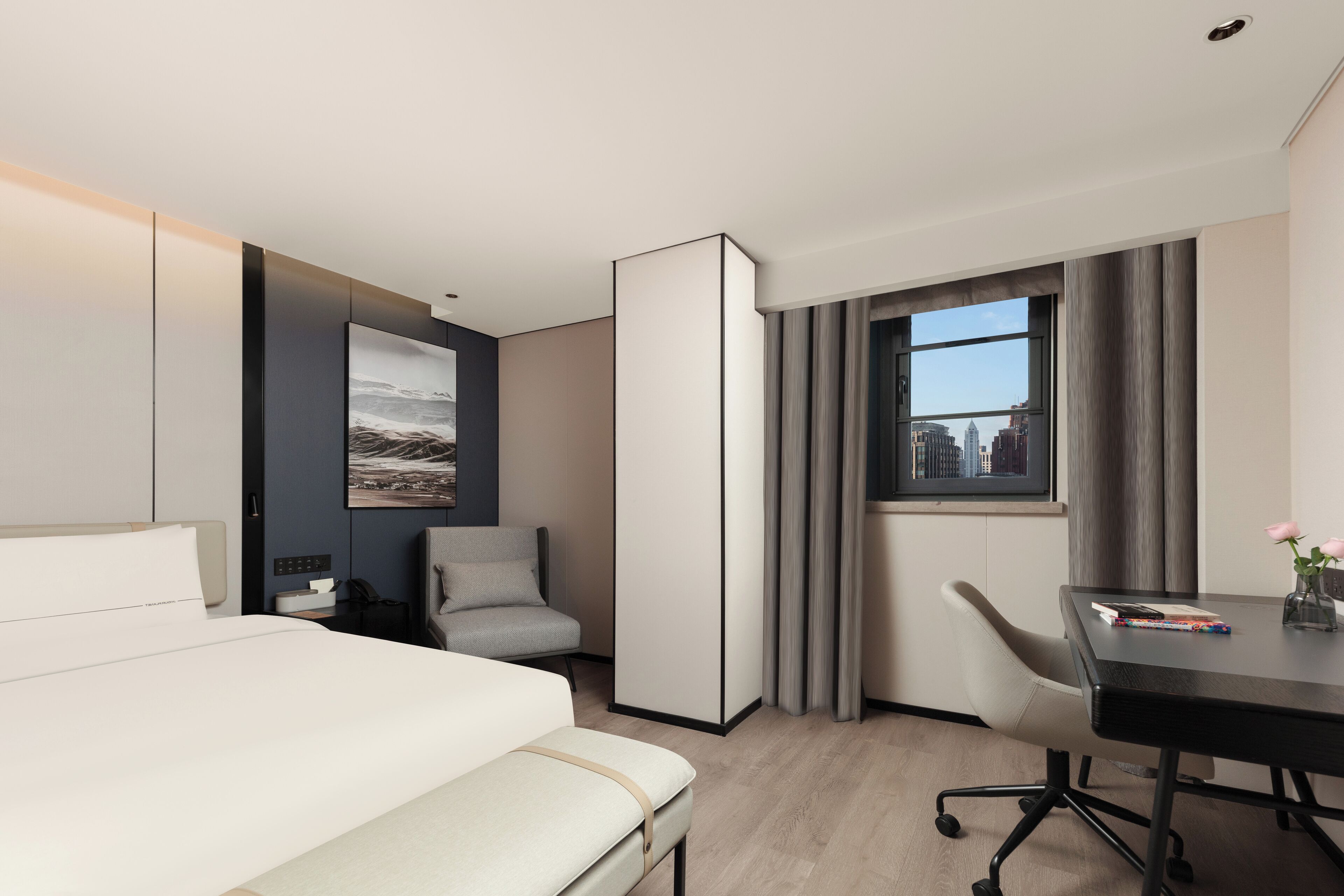 Una habitación de hotel moderna con una cama, un escritorio, una silla, vistas de la ciudad a través de una ventana y un cuadro de un paisaje urbano en la pared.