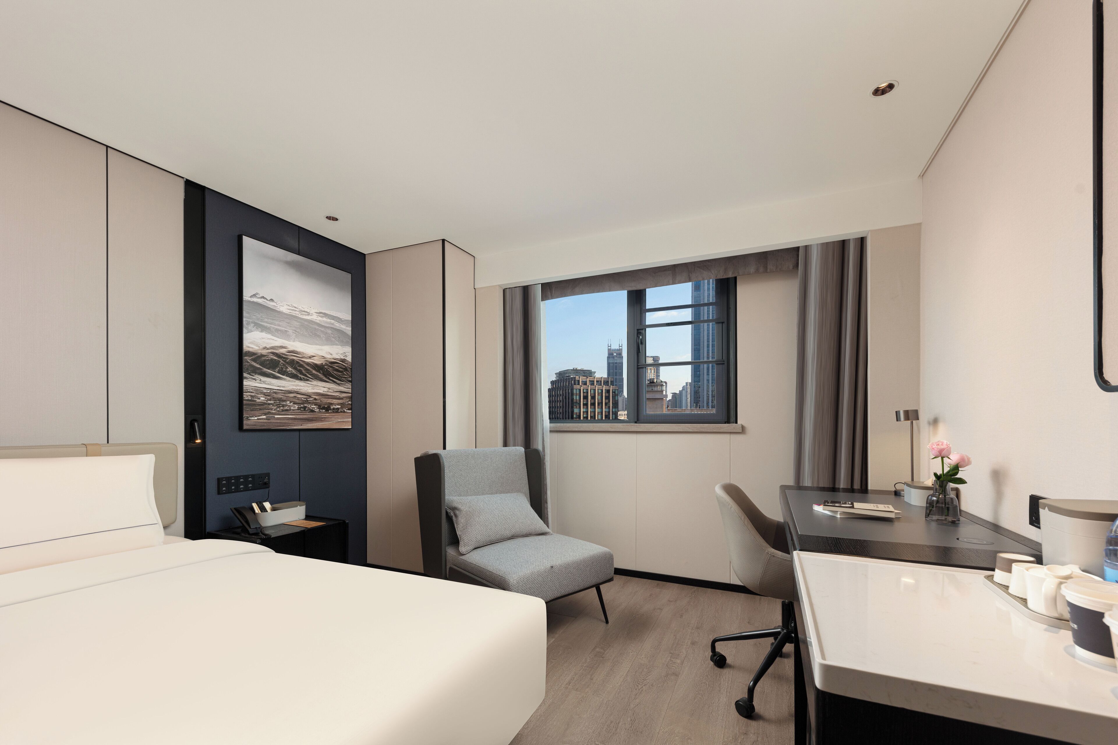 Habitación de hotel moderna con una cama, un escritorio, una silla, un ventanal con vista a la ciudad y un cuadro enmarcado en la pared.