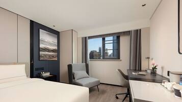 Habitación de hotel moderna con una cama, un escritorio, una silla, un ventanal con vista a la ciudad y un cuadro enmarcado en la pared.
