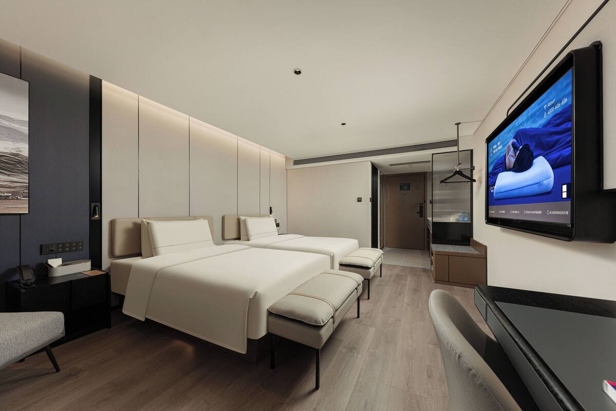 Une chambre d’hôtel moderne équipée de deux lits, d’une télévision et d’un bureau.