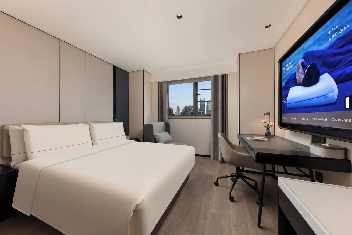 Une chambre d’hôtel moderne, dotée d’un grand lit, d’un bureau et d’un téléviseur diffusant une publicité pour des chaussures.
