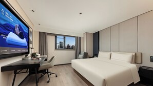 Ein modernes Hotelzimmer mit einem großen Bett, einem Schreibtisch mit Stuhl, einem Fernseher und einem Fenster mit Blick auf die Stadt.