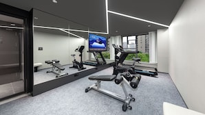 Ein modernes Fitnessstudio mit Trainingsgeräten, einem großen Spiegel und einem Fernseher, der ein Trainingsvideo zeigt.