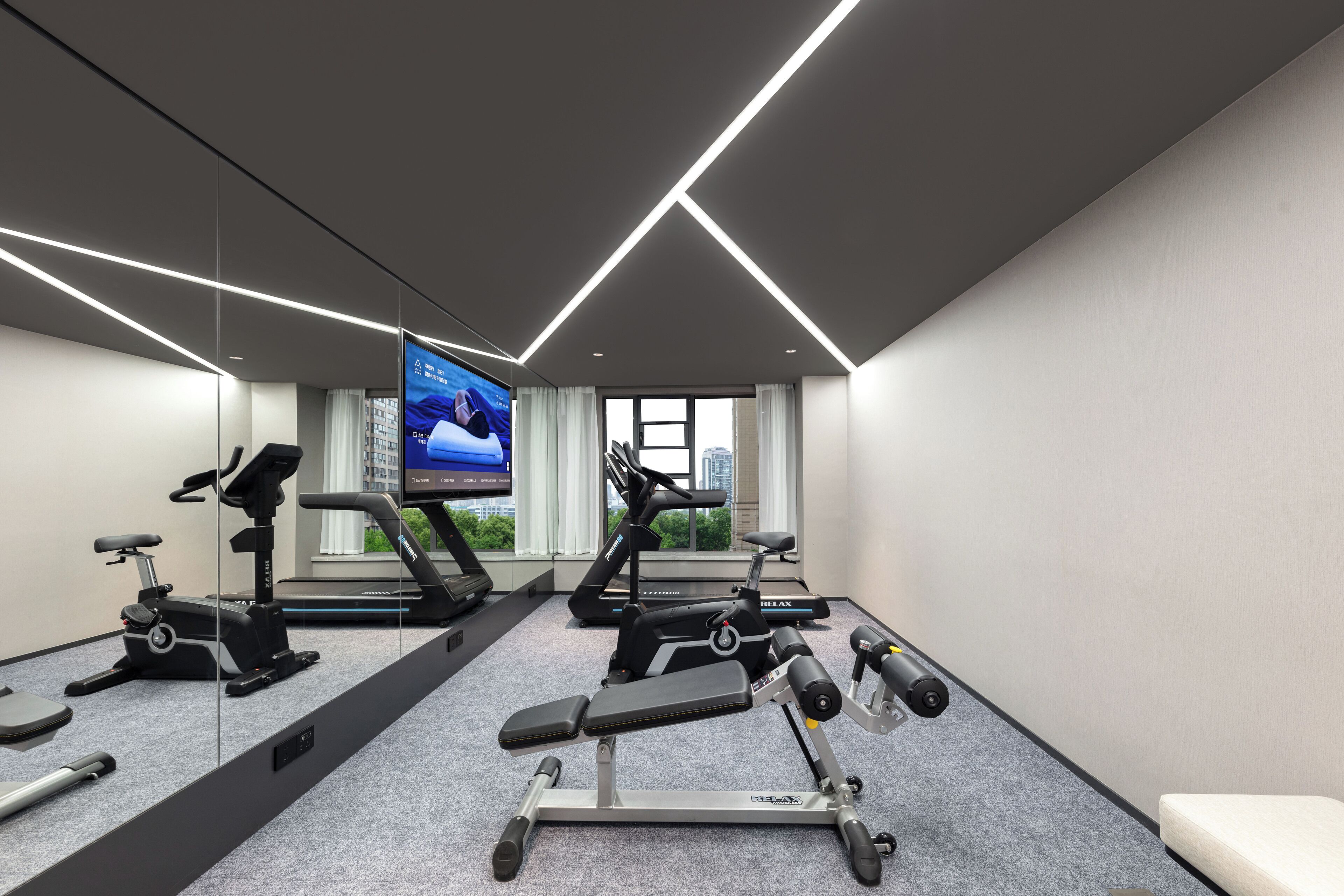 Een moderne sportschool met fitnessapparatuur, een grote spiegel en een televisiescherm.