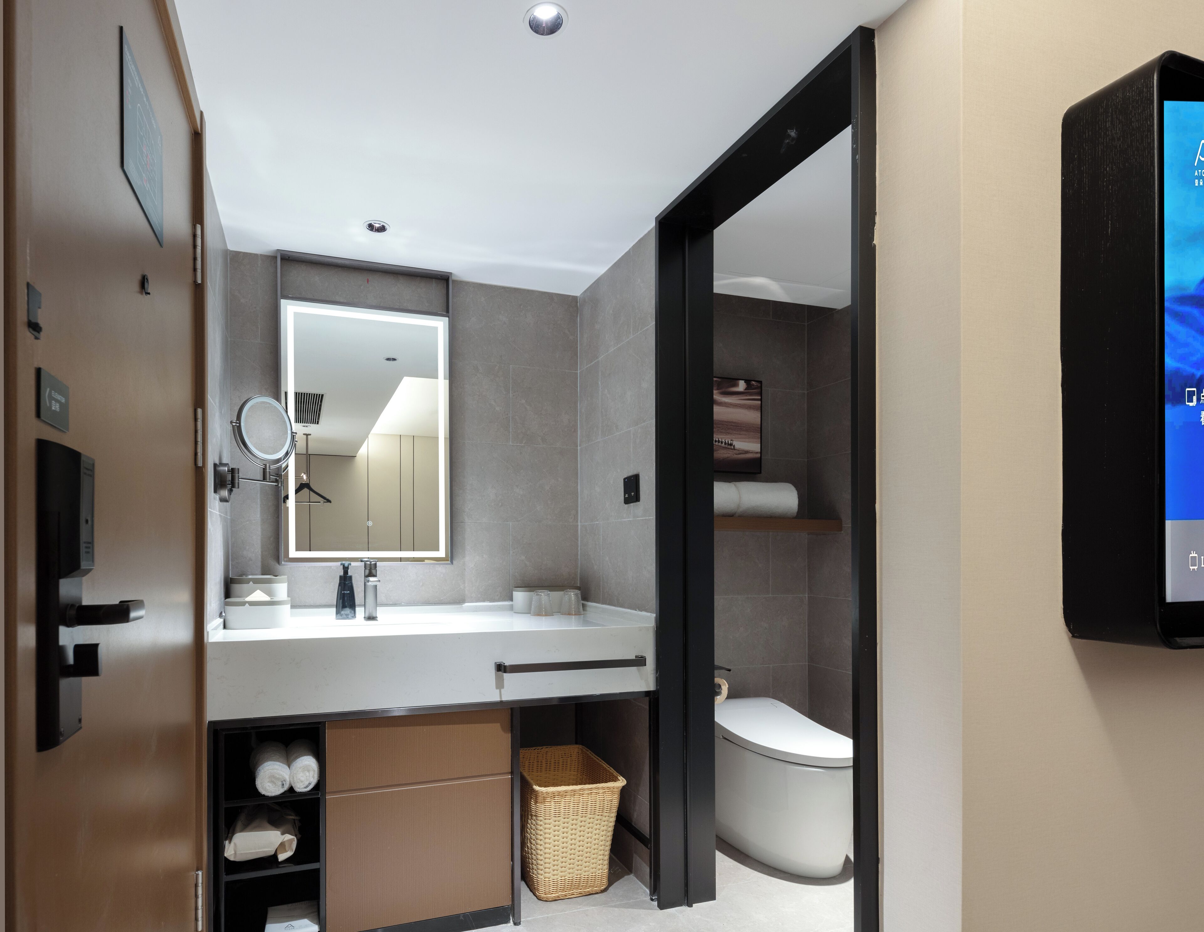 Un baño moderno con un espejo grande, un inodoro y un lavabo. Hay una cesta debajo del lavabo y un estante sobre el inodoro.