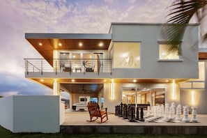 A modern two-story house with a balcony, a large chess set, and a rocking chair. - 6k Sq Ft of Luxury Mountain View’s over the Pacific Ocean in SJDS! (San Juan Del Sur)