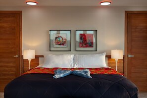 Habitación de hotel con una cama grande, dos lámparas de pared y dos cuadros enmarcados sobre la cama.