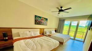 A hotel room with two beds, a ceiling fan, a painting, and a balcony with a view.