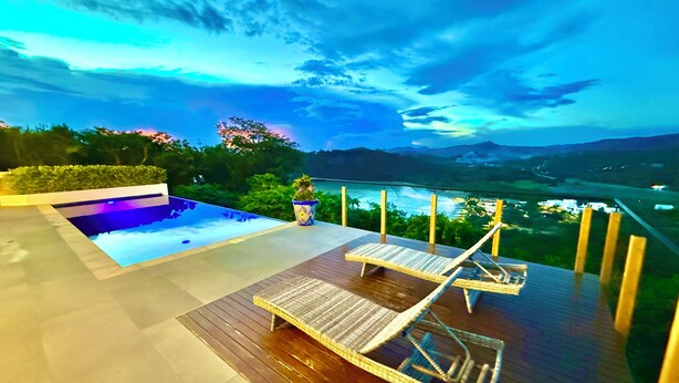 A deck with two lounge chairs, a small pool, and a view of a valley and mountains.