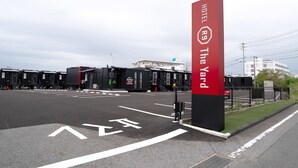 En hotellentréd med en framträdande röd skylt, en parkeringsplats och en byggnad i bakgrunden.