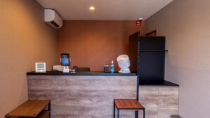 Ett receptionsområde med en trädisk, en digital skärm, en liten fläkt och två trästolar.