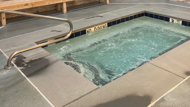 Zona de piscina con un cartel de 'NO DIVING', bancos de madera y paredes de piedra.