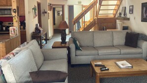 Una sala de estar acogedora con un sofá, una mesa de centro y una lámpara. Se ve una escalera que sube a un nivel superior.