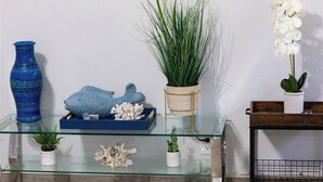 Eine Glastrennwand mit dekorativen Gegenständen, darunter eine blaue Vase, eine Fischskulptur, eine Pflanze und eine weiße Orchidee.