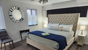 Ein Schlafzimmer mit einem großen Bett, einem Sessel, einem Nachttisch mit Lampe und einer Wanduhr.