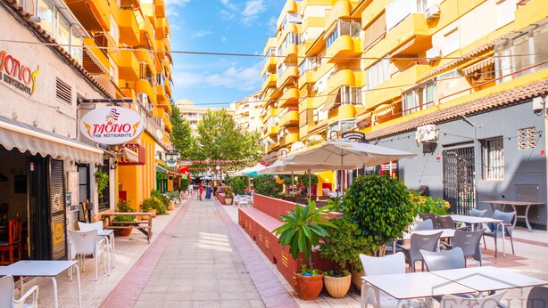 Une rue bordée d’immeubles jaunes, avec des terrasses et des plantes en pot.