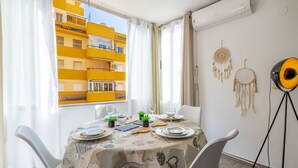 Un coin repas avec une table dressée pour quatre personnes, une vue sur un bâtiment jaune et des attrape-rêves accrochés au mur.