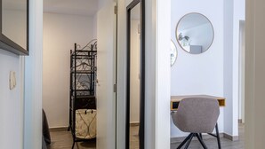 Un couloir avec un plancher en bois, un présentoir en métal noir et une chaise grise.