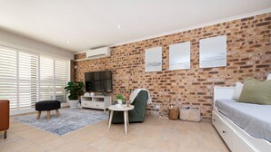 A modern living room with a brick wall, a flat-screen TV, a sofa, a coffee table, and a chair. - Nelson Bay Family Retreat (Nelson Bay)