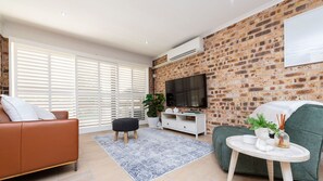 A modern living room with a brick wall, a flat-screen TV, a sofa, a coffee table, and a potted plant.