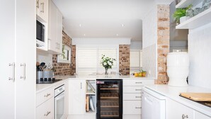 A modern kitchen with white cabinetry, a brick accent wall, and a dishwasher. - Nelson Bay Family Retreat (Nelson Bay)