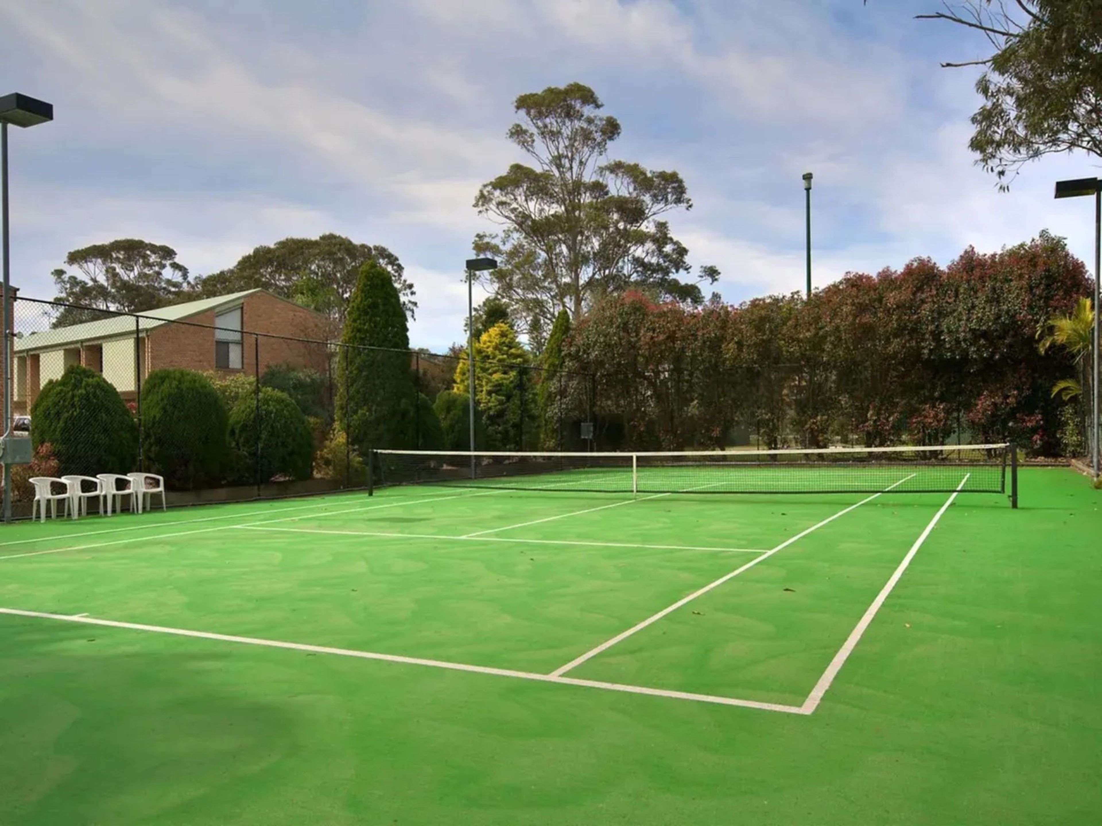 An outdoor tennis court with a net, surrounded by trees and a fence.