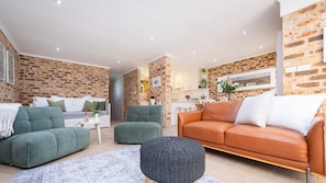 A modern living room with a brick wall, green sofas, an orange leather sofa, and a round ottoman.