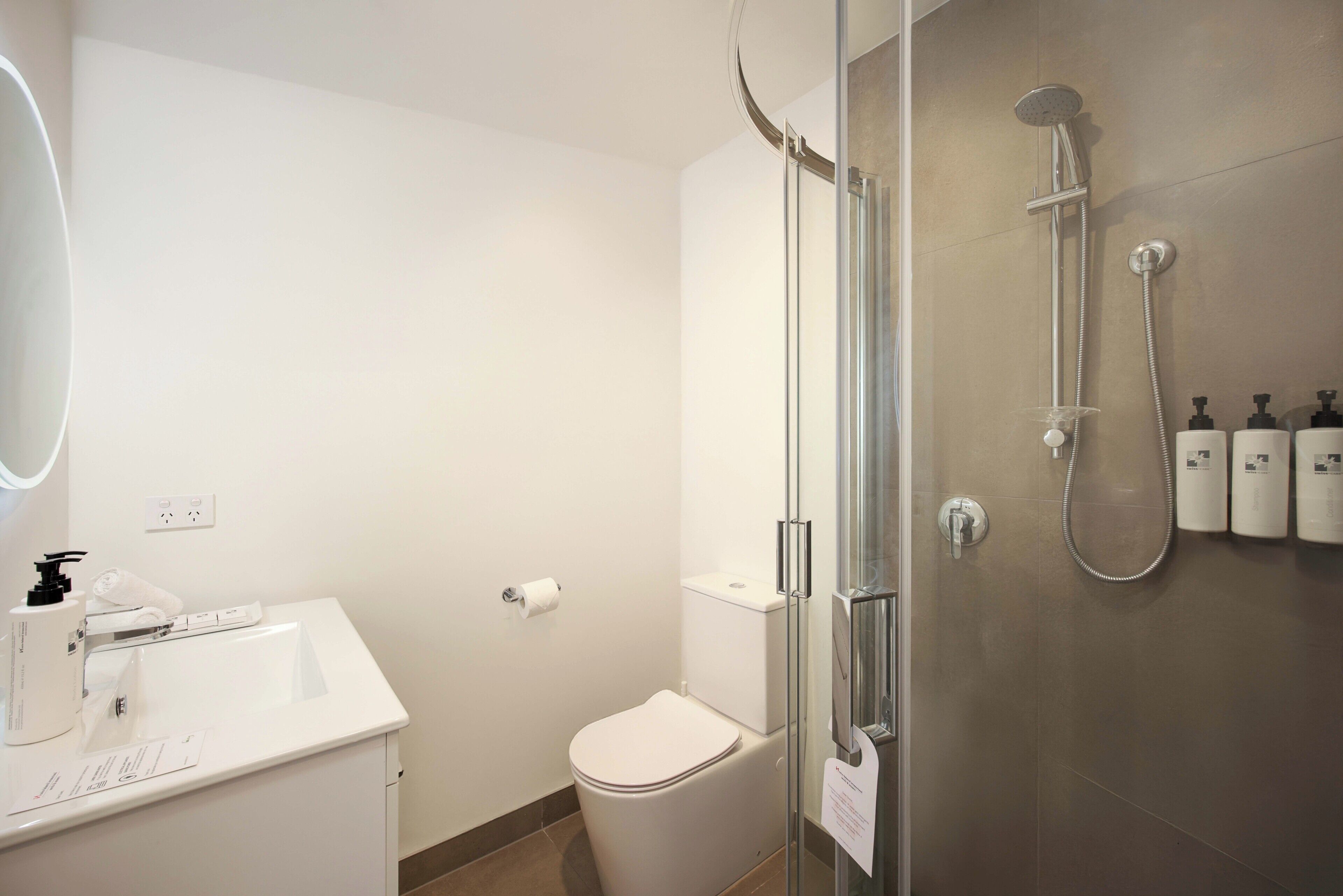 Ett modernt badrum med en dusch som är avskärmad med glasväggar, en vit tvättställ och hygienartiklar på väggen.