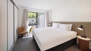 Een moderne hotelkamer met een groot bed, een stoel, een nachtkastje met lamp en uitzicht op het groen door een groot raam.