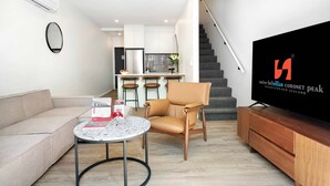 Een moderne woonkamer met een bank, een rond bijzettafeltje, een leren fauteuil, een flatscreen-tv en een trap die naar de keuken leidt.