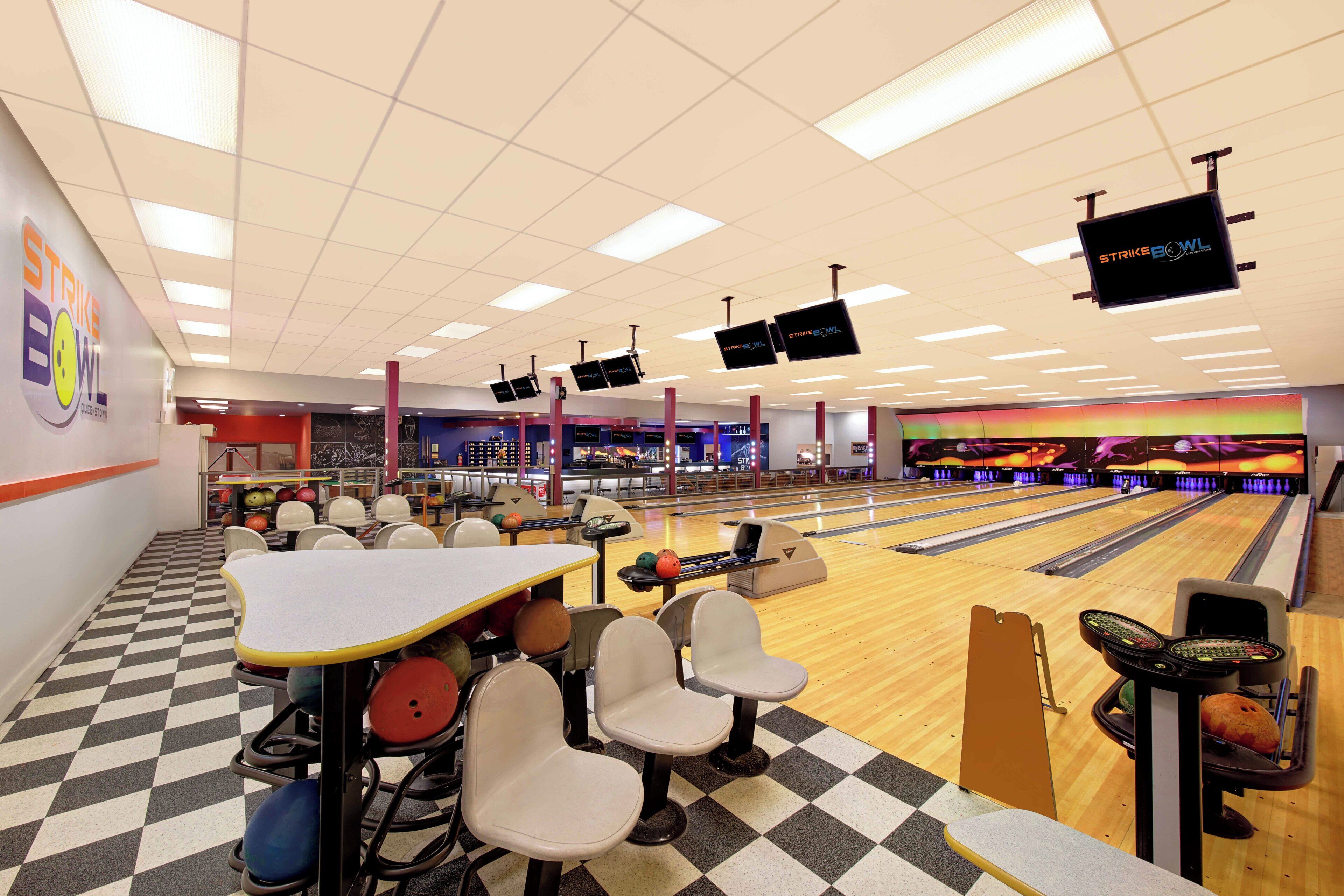 A bowling alley with multiple lanes, bowling balls, and seating areas.