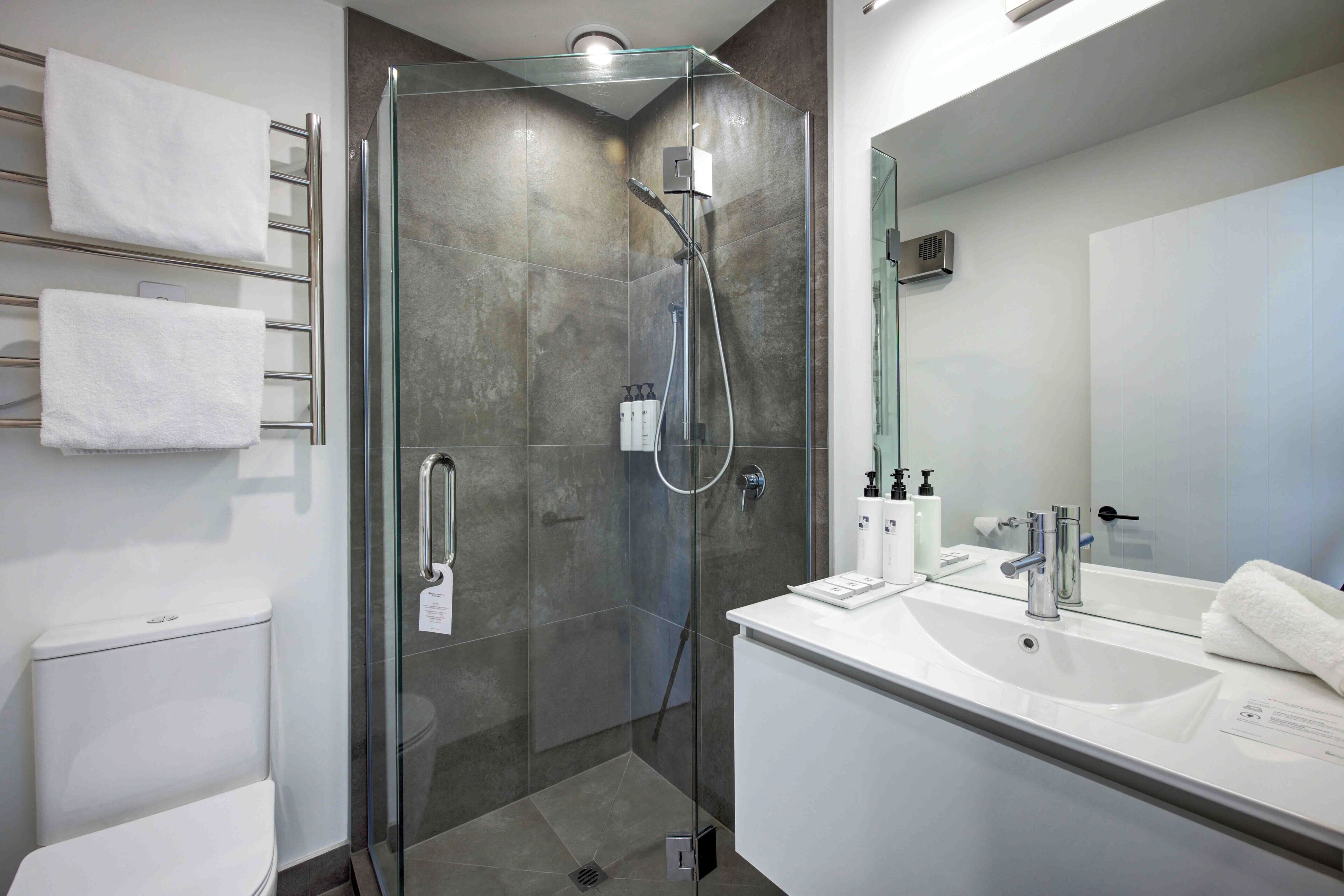 A modern bathroom with a glass-enclosed shower, a white sink with a mirror, and a towel rack with white towels.
