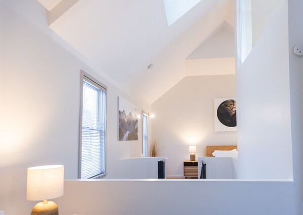 Une chambre à coucher moderne avec une lucarne, des murs blancs et un lit doté d’une tête de lit en bois.