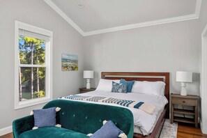 A bedroom with a bed, two bedside tables, a window with a view of trees, and a green armchair.