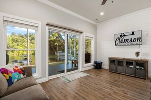 A spacious room with a large sliding glass door leading to a deck, a wooden floor, a brown sofa, and a wall-mounted sign.