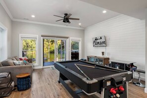 A pool table in a room with a ceiling fan, a couch, and a sign reading 'Clemson Vacation Rentals.'