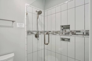 Une salle de bain moderne avec des carreaux blancs, une douche équipée d’un pommeau de douche à main et un petit miroir.