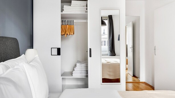 A modern hotel room with a neatly made bed, a large wardrobe with folded clothes, and a visible bathroom door. - Blueground | Alsergrund, rooftop, nr Votivkirche (Vienna)