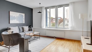 A modern living room with a grey sofa, a coffee table, a chair, a TV, and a large window with curtains. - Blueground | Alsergrund, rooftop, nr Votivkirche (Vienna)