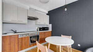 A compact kitchen with white cabinets, a built-in oven, a coffee maker, and a microwave. There is a round table with two chairs. - Blueground | Alsergrund, rooftop, nr Votivkirche (Vienna)