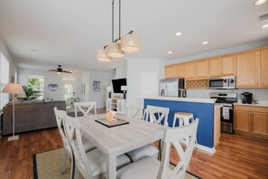 A modern kitchen with wooden cabinets, a central island, and a dining area with white chairs and a table.