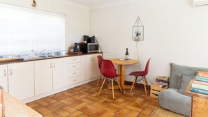 A compact kitchen with white cabinets, a wooden dining table, and red chairs. A microwave and kettle are on the counter. - Rustic, cosy one bedroom guesthouse. Just a short walk to Umina Beach! (Umina Beach)