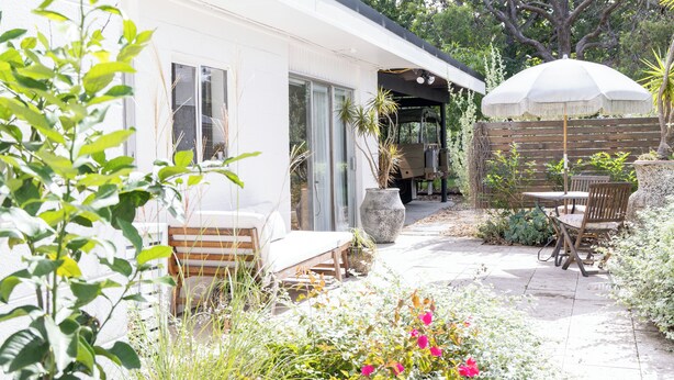 A patio area with a white building, outdoor furniture, and a large umbrella. - Rustic, cosy one bedroom guesthouse. Just a short walk to Umina Beach! (Umina Beach)