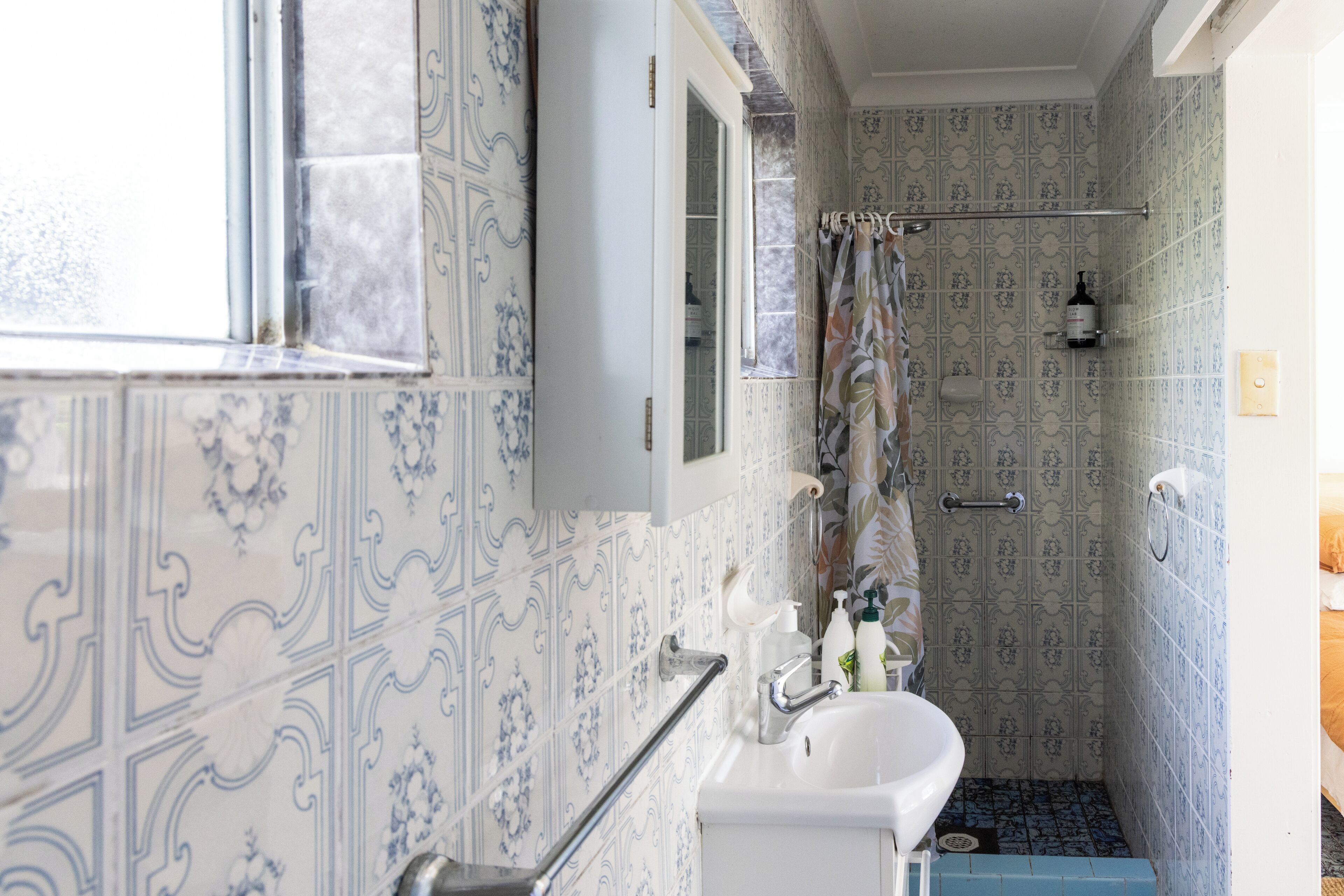 A bathroom with patterned tiles, a white sink, a mirror, and a shower area.